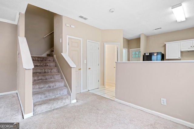 interior space with black refrigerator, light carpet, white cabinets, and a textured ceiling