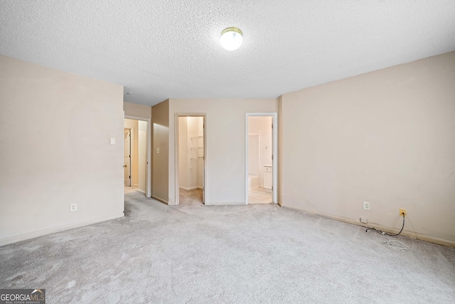 unfurnished bedroom featuring ensuite bathroom, a textured ceiling, a spacious closet, light colored carpet, and a closet