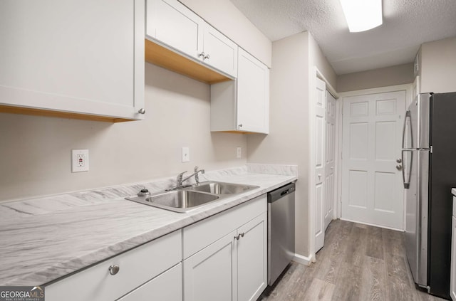 kitchen featuring light hardwood / wood-style floors, stainless steel appliances, a textured ceiling, white cabinetry, and sink