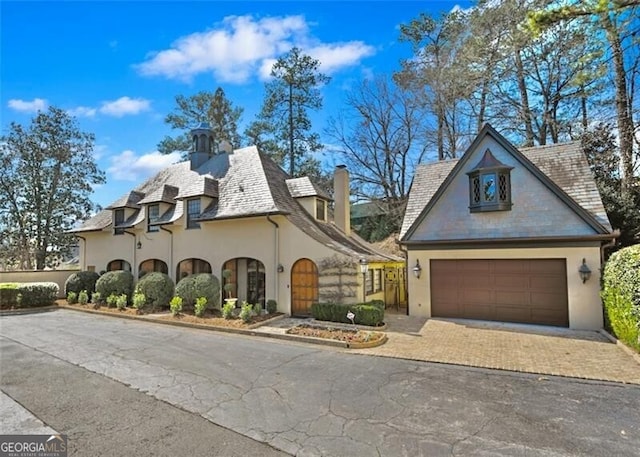 view of front facade featuring a garage, decorative driveway, a chimney, and stucco siding