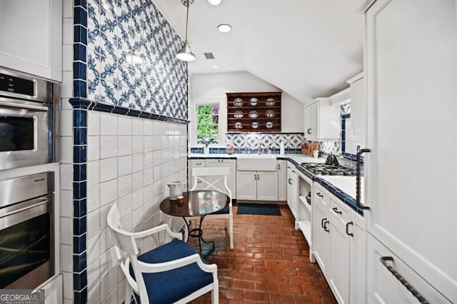 kitchen featuring a sink, brick floor, vaulted ceiling, white cabinetry, and tile walls