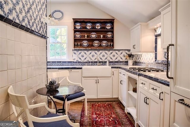 kitchen featuring stainless steel gas cooktop, open shelves, tile counters, lofted ceiling, and white cabinets