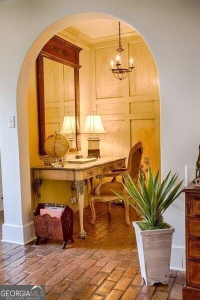 living area featuring a chandelier, arched walkways, brick floor, and baseboards