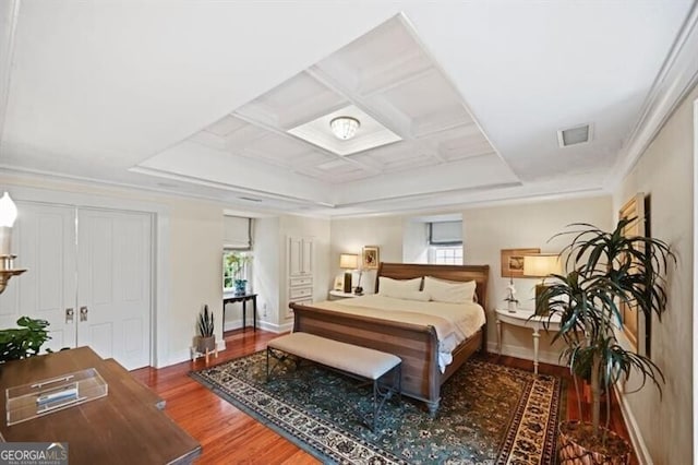 bedroom with visible vents, baseboards, coffered ceiling, wood finished floors, and crown molding