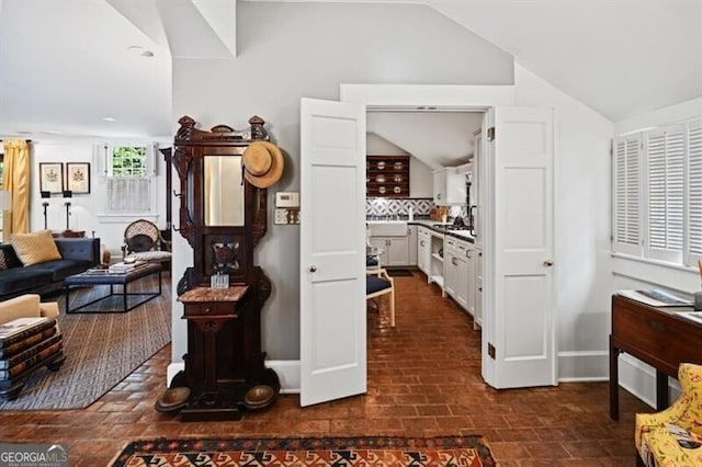 living room featuring brick floor, lofted ceiling, and baseboards