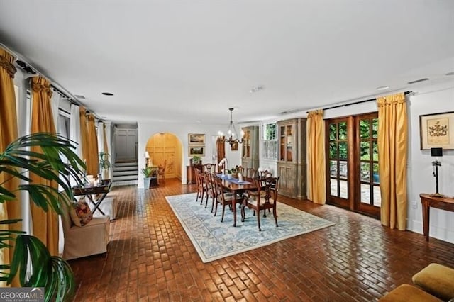 dining room with brick floor, stairs, arched walkways, and a notable chandelier