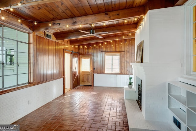 interior space with wooden ceiling, a barn door, wood walls, ceiling fan, and a brick fireplace