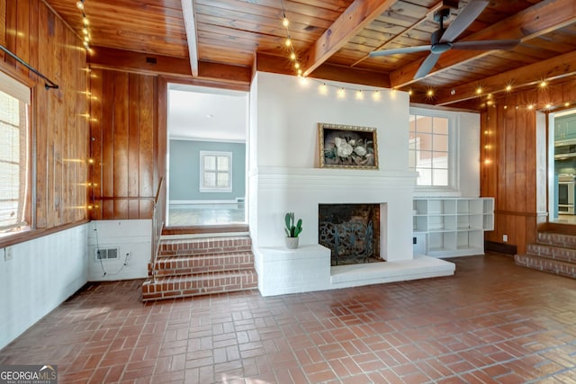 unfurnished living room featuring wooden walls, plenty of natural light, wood ceiling, and beam ceiling