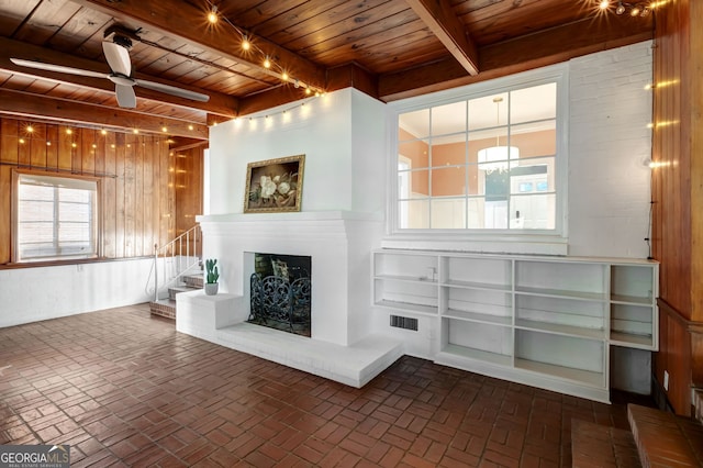 unfurnished living room featuring beamed ceiling, wood walls, ceiling fan, and wood ceiling