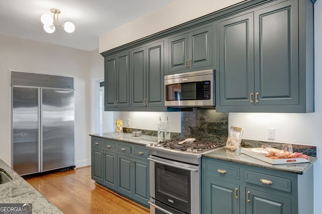 kitchen featuring light stone counters, light hardwood / wood-style floors, an inviting chandelier, blue cabinets, and appliances with stainless steel finishes