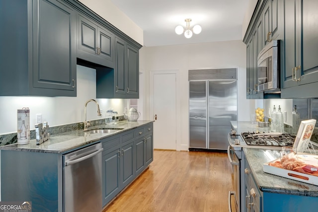 kitchen with stainless steel appliances, dark stone countertops, sink, and light wood-type flooring