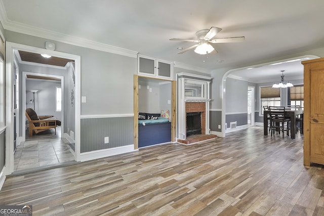 living room with ceiling fan with notable chandelier, a fireplace, hardwood / wood-style flooring, and crown molding