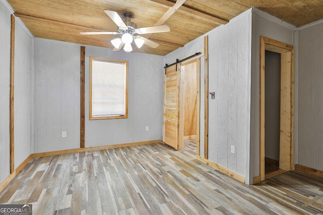 unfurnished bedroom with wood walls, light hardwood / wood-style floors, wood ceiling, a barn door, and ceiling fan