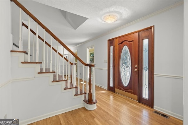 foyer entrance featuring light hardwood / wood-style floors, a textured ceiling, and ornamental molding