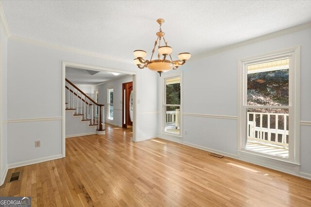 unfurnished dining area with crown molding, an inviting chandelier, a textured ceiling, and light hardwood / wood-style floors