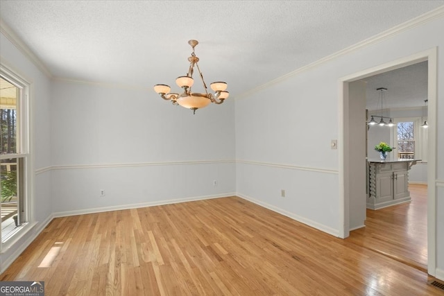 empty room with crown molding, an inviting chandelier, and plenty of natural light