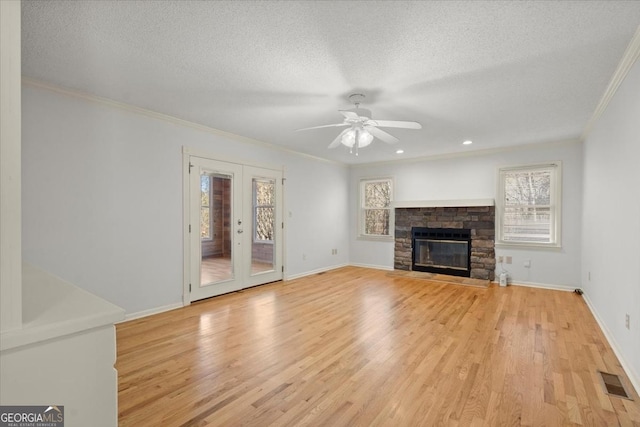 unfurnished living room with a wealth of natural light, light hardwood / wood-style flooring, ornamental molding, and a stone fireplace