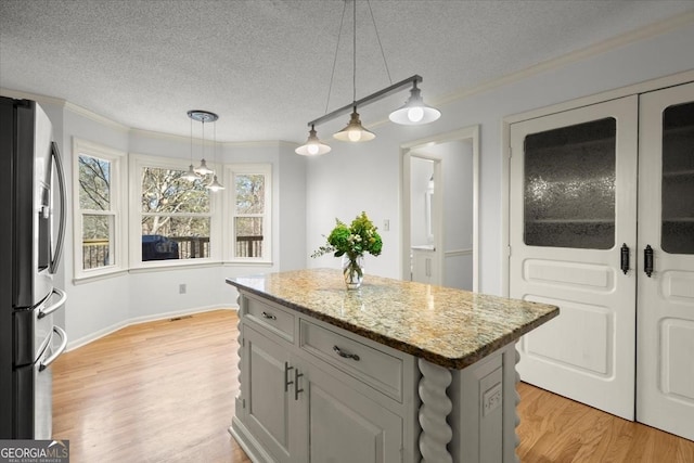 kitchen with a kitchen island, light hardwood / wood-style floors, stainless steel fridge, light stone counters, and crown molding