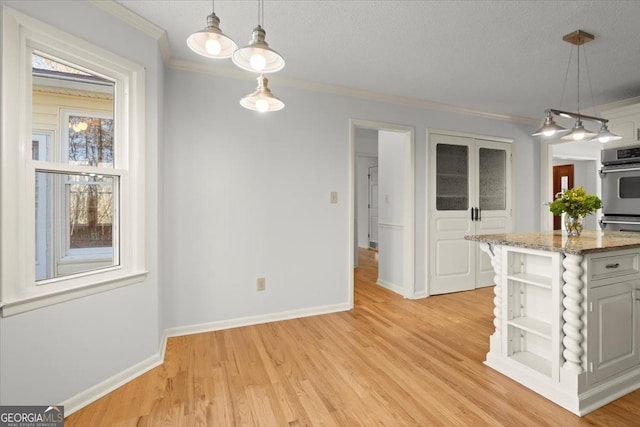 kitchen featuring decorative light fixtures, light stone countertops, crown molding, and light wood-type flooring