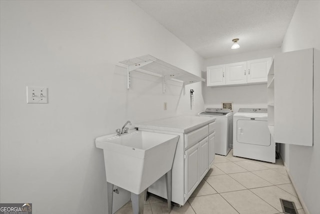 washroom featuring a textured ceiling, sink, washer and dryer, cabinets, and light tile patterned flooring