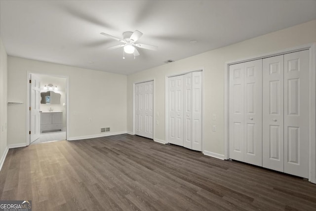 unfurnished bedroom featuring ceiling fan, dark hardwood / wood-style floors, two closets, and ensuite bathroom