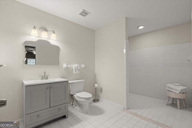 bathroom with a tile shower, toilet, tile patterned flooring, and vanity