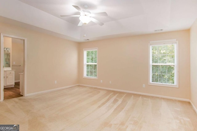 empty room featuring ceiling fan, a tray ceiling, light carpet, and plenty of natural light