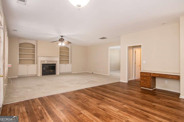 unfurnished living room with built in features, ceiling fan, and wood-type flooring