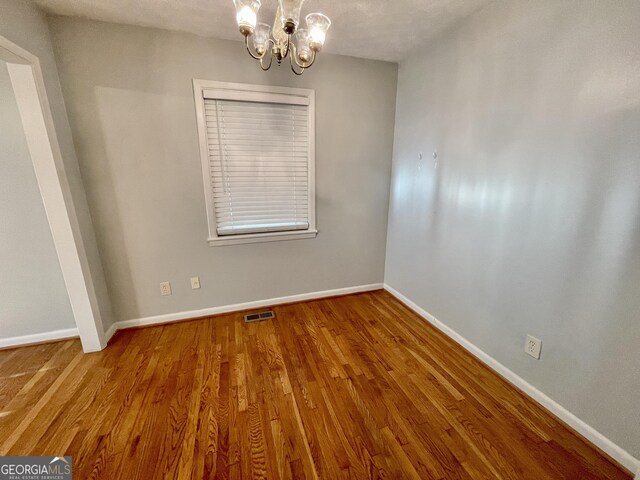 empty room with a notable chandelier, a textured ceiling, and hardwood / wood-style flooring