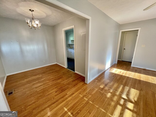 empty room with a textured ceiling, hardwood / wood-style floors, and a notable chandelier