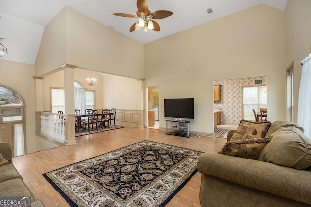 living room with ceiling fan with notable chandelier, high vaulted ceiling, plenty of natural light, and light hardwood / wood-style flooring