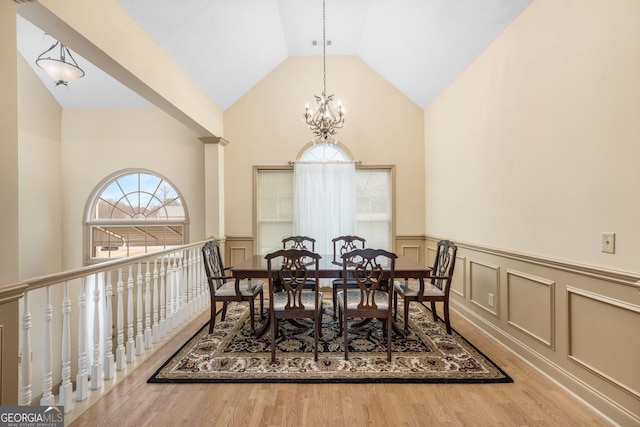 dining area featuring high vaulted ceiling, wood finished floors, wainscoting, a decorative wall, and an inviting chandelier