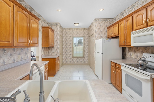 kitchen featuring a sink, light countertops, wallpapered walls, and white appliances