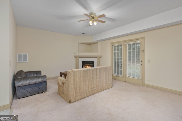 carpeted living area with baseboards, a lit fireplace, visible vents, and a ceiling fan