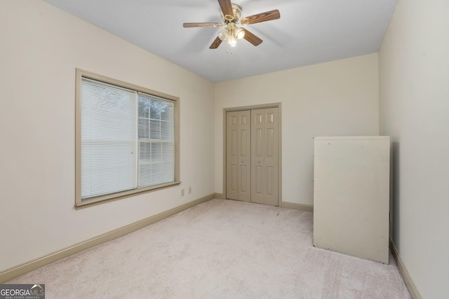 unfurnished bedroom featuring light carpet, baseboards, a closet, and a ceiling fan
