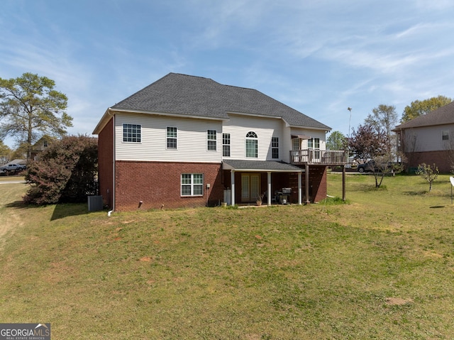 back of property featuring a wooden deck, brick siding, roof with shingles, cooling unit, and a yard