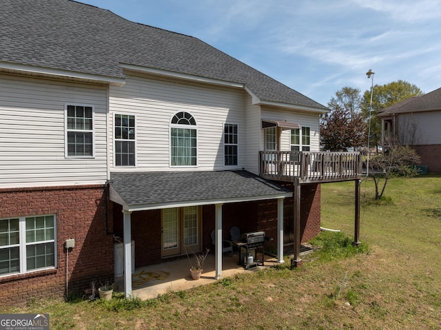 rear view of property featuring a deck, brick siding, roof with shingles, a yard, and a patio area
