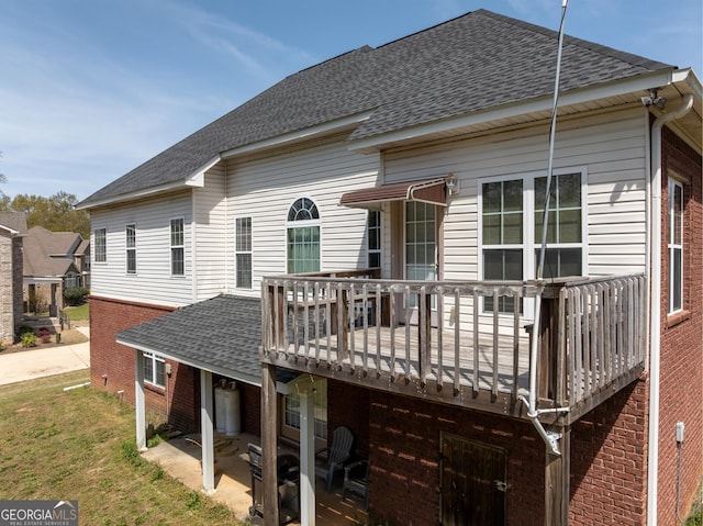 back of house featuring brick siding, a wooden deck, a yard, and roof with shingles