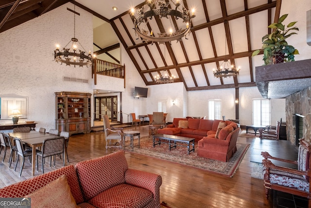 living room with high vaulted ceiling, hardwood / wood-style floors, a notable chandelier, and a stone fireplace