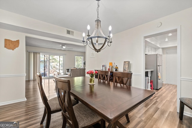 dining area with a raised ceiling, ceiling fan with notable chandelier, and wood-type flooring