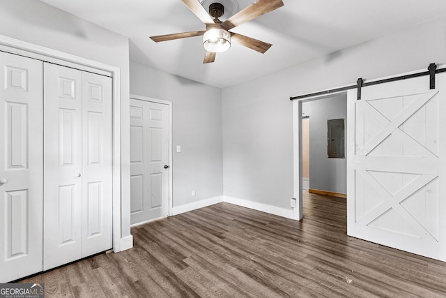 unfurnished bedroom featuring electric panel, ceiling fan, a closet, a barn door, and dark hardwood / wood-style floors