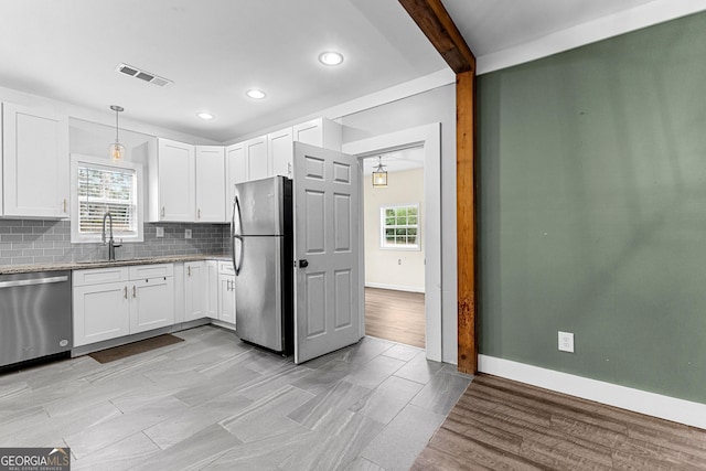 kitchen featuring appliances with stainless steel finishes, light stone countertops, pendant lighting, sink, and white cabinetry