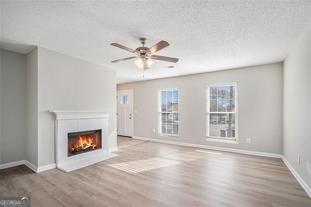 unfurnished living room featuring a textured ceiling, a fireplace, ceiling fan, and light hardwood / wood-style floors