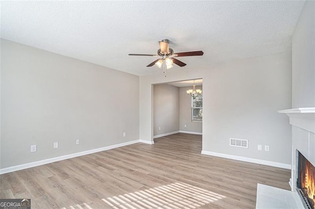 unfurnished living room with a textured ceiling, light hardwood / wood-style flooring, and ceiling fan with notable chandelier