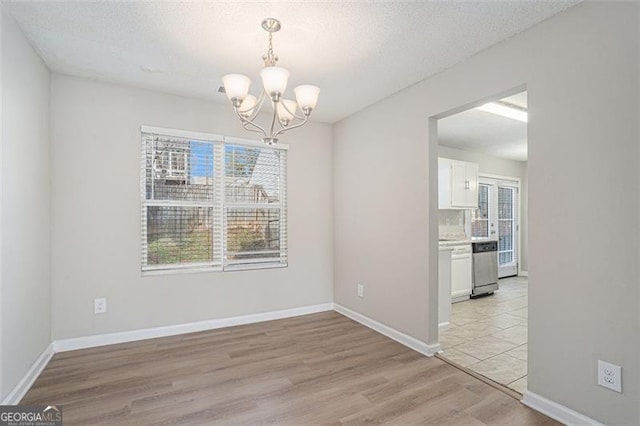 unfurnished dining area featuring a wealth of natural light, a textured ceiling, light hardwood / wood-style floors, and a chandelier