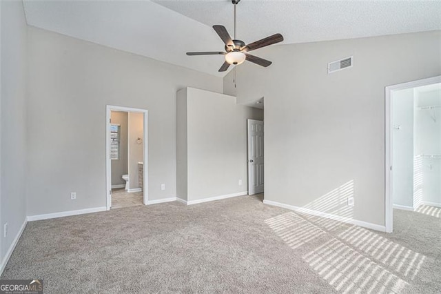 unfurnished bedroom with ensuite bath, a closet, a walk in closet, ceiling fan, and light carpet