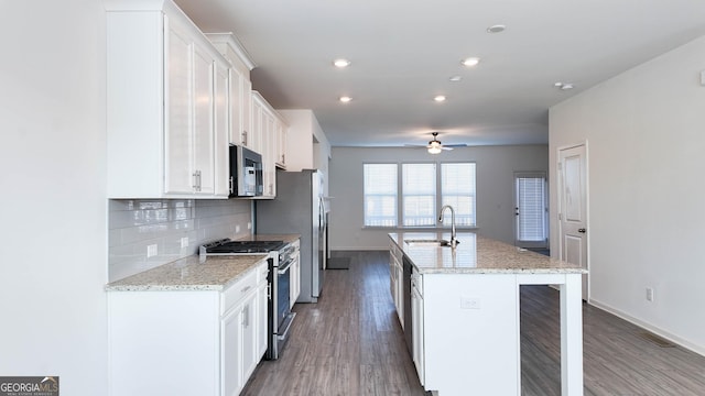 kitchen with light stone counters, a center island with sink, white cabinets, appliances with stainless steel finishes, and sink