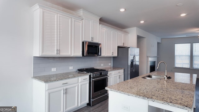 kitchen featuring light stone countertops, tasteful backsplash, a kitchen island with sink, white cabinetry, and appliances with stainless steel finishes