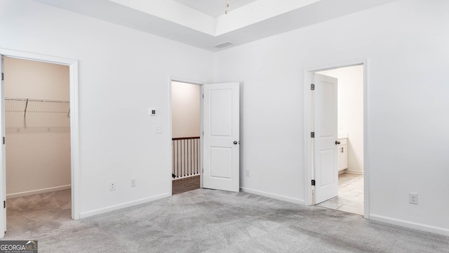 unfurnished bedroom featuring a spacious closet, a closet, and light carpet