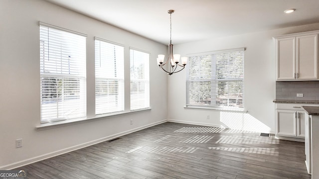 unfurnished dining area featuring an inviting chandelier, a healthy amount of sunlight, and dark hardwood / wood-style floors